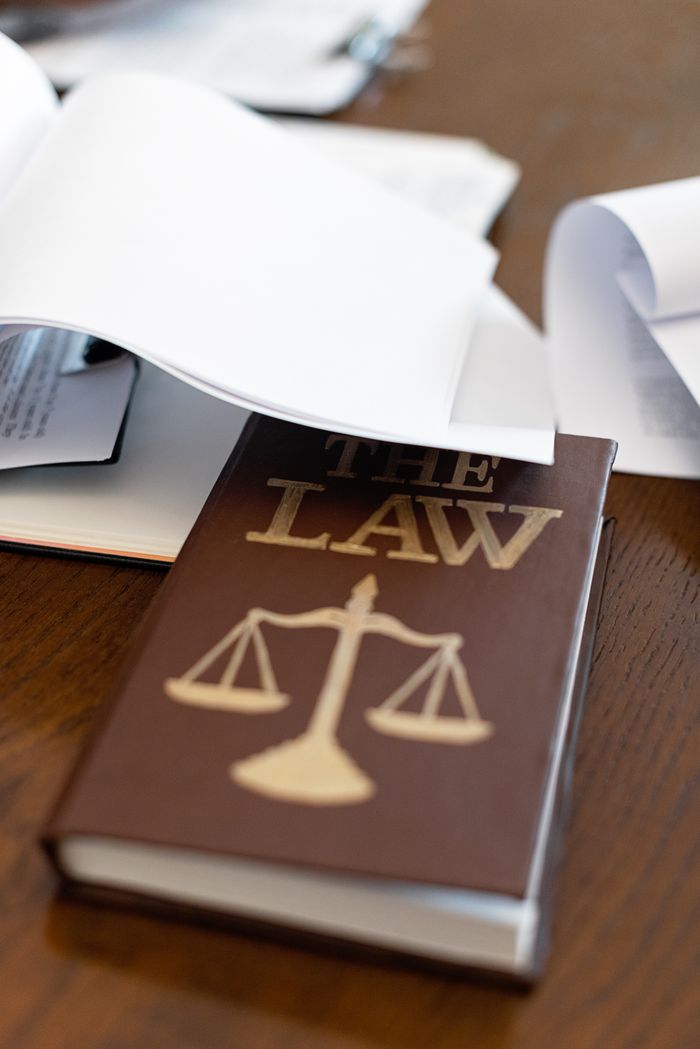 Offerings Close-up of a law book with scales icon on a wooden desk covered in papers.